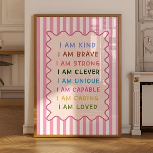 May include: A framed wall art print featuring a pink and white vertical striped background. A central light pink scalloped rectangle contains the text: I AM KIND, I AM BRAVE, I AM STRONG, I AM CLEVER, I AM UNIQUE, I AM CAPABLE, I AM CARING, I AM LOVED.