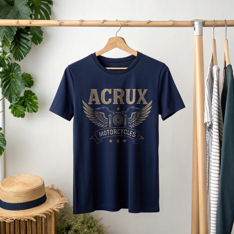 May include: A navy blue short-sleeve t-shirt featuring a graphic print on the chest. The design includes the text ACRUX in a distressed font above a stylized motorcycle emblem with wings, the word MOTORCYCLES on a banner, and three small stars.
