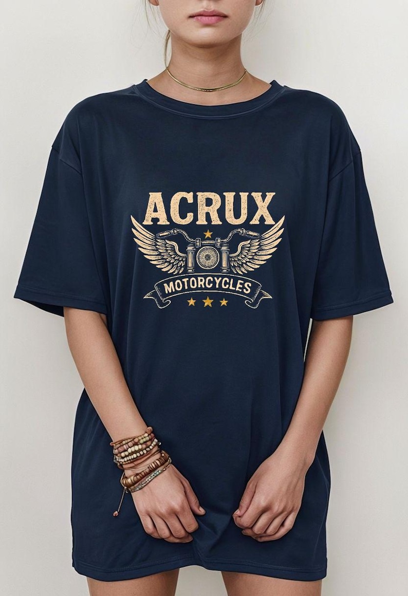 May include: A navy blue short-sleeve t-shirt featuring a graphic print in light yellow. The design includes the text ACRUX above a stylized motorcycle emblem with wings, the word MOTORCYCLES on a banner, and three small stars at the bottom.