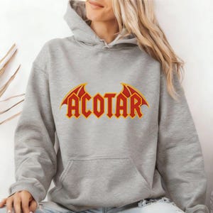 Light gray hoodie with bold red and yellow 'ACOTAR' lettering and bat-wing graphics, styled as fan merch for lovers of 'A Court of Thorns and Roses' — cozy apparel for fantasy readers and bookish introverts drawn to gothic motifs and high-fae lore.