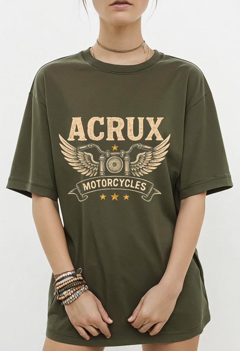 May include: An olive green short-sleeve t-shirt featuring a graphic print in light yellow. The design includes the text ACRUX, a stylized motorcycle handlebar with wings, the word MOTORCYCLES on a banner, and three small stars below the banner.