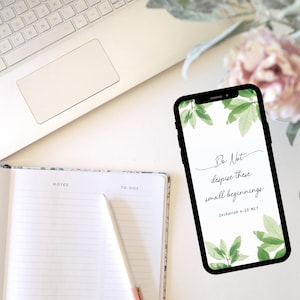 Peut inclure: Un ordinateur portable blanc, un carnet, un stylo et un smartphone avec un &eacute;tui noir. L'&eacute;cran du t&eacute;l&eacute;phone affiche une citation de la Bible : &laquo; Ne m&eacute;prisez pas ces petits commencements. &raquo; Zacharie 4:10 NLT. L'arri&egrave;re-plan est une surface blanche avec une fleur rose.