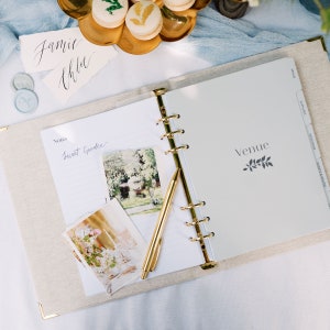 The wedding planner is laid open on a table to show the venue divider and notes page. The wedding planner notes page has a photo of venues stuck inside for inspiration with some decorative wax seals.
