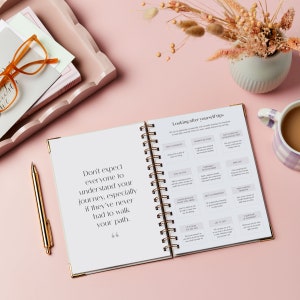 The IVF planner is laid open on a pink background to reveal some looking after yourself tips. The journal is laid flat.