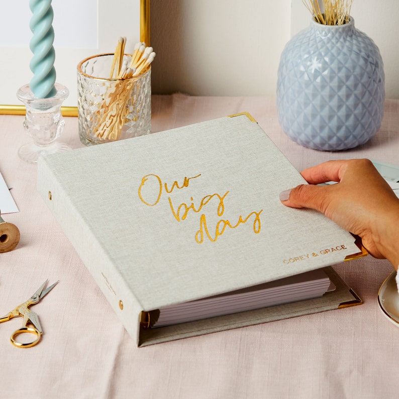 A personalised wedding planner and organiser in a stone linen with the phrase 'our big day' in a cursive font. The bottom right hand corner is personalised with the names COREY & GRACE. The wedding planner is on a desk.