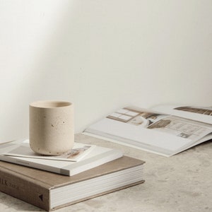 May include: A stack of three books with a concrete cup on top. The top book has the word "Copenhagen" printed on the spine. The bottom book has the word "Table" printed on the spine.