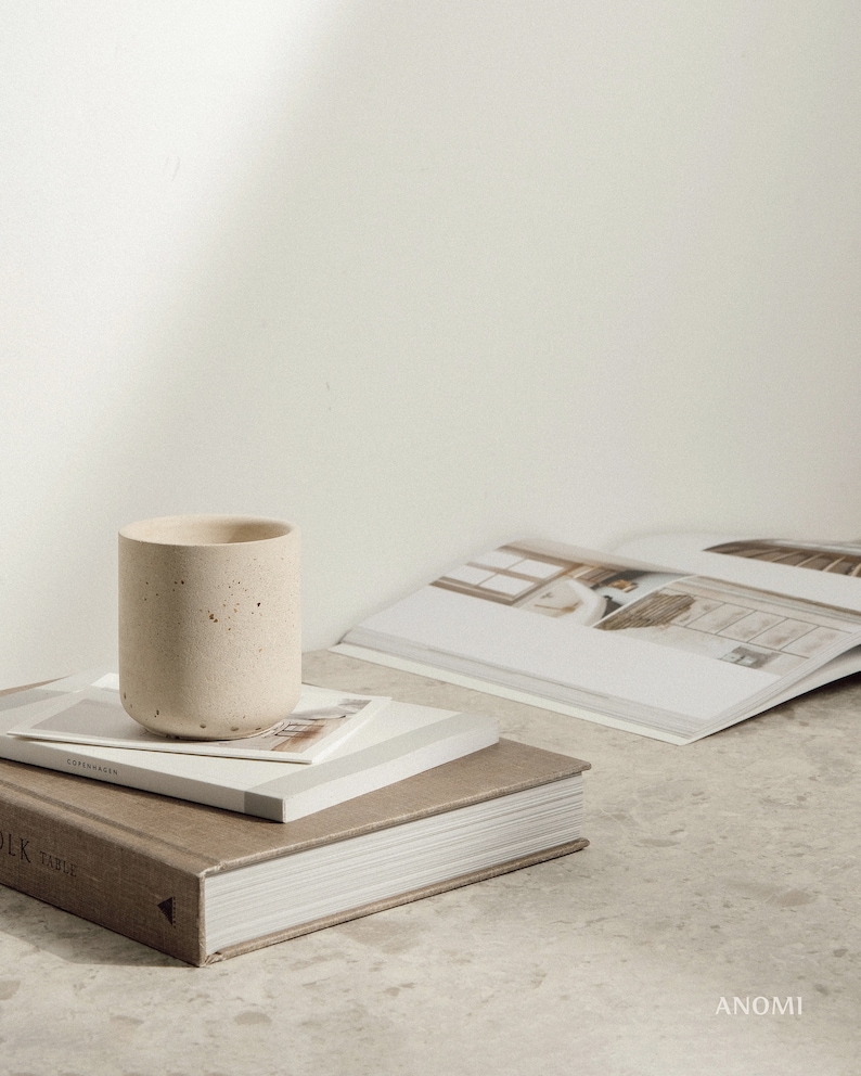 May include: A stack of three books with a concrete cup on top. The top book has the word "Copenhagen" printed on the spine. The bottom book has the word "Table" printed on the spine.
