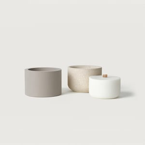 Può includere: Tre contenitori minimalisti in ceramica in una palette di colori neutri. Un vaso grigio cilindrico, un vaso beige maculato e un piccolo vaso bianco con coperchio in legno. Per l'arredamento della casa.