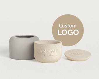 May include: A set of three neutral-toned ceramic containers. One is a cylindrical gray pot, another is a beige pot with the text "ANOMI STUDIO", and a matching lid. A tan circle with "Custom LOGO" is in the background.