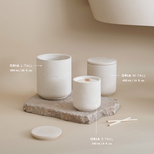May include: Three white ceramic candles of varying sizes with wooden wicks. The candles are labelled "ORIA L-TALL 800 ml / 28 fl. oz.", "ORIA M-TALL 450 ml / 16 fl. oz.", and "ORIA S-TALL 240 ml / 8 fl. oz.".
