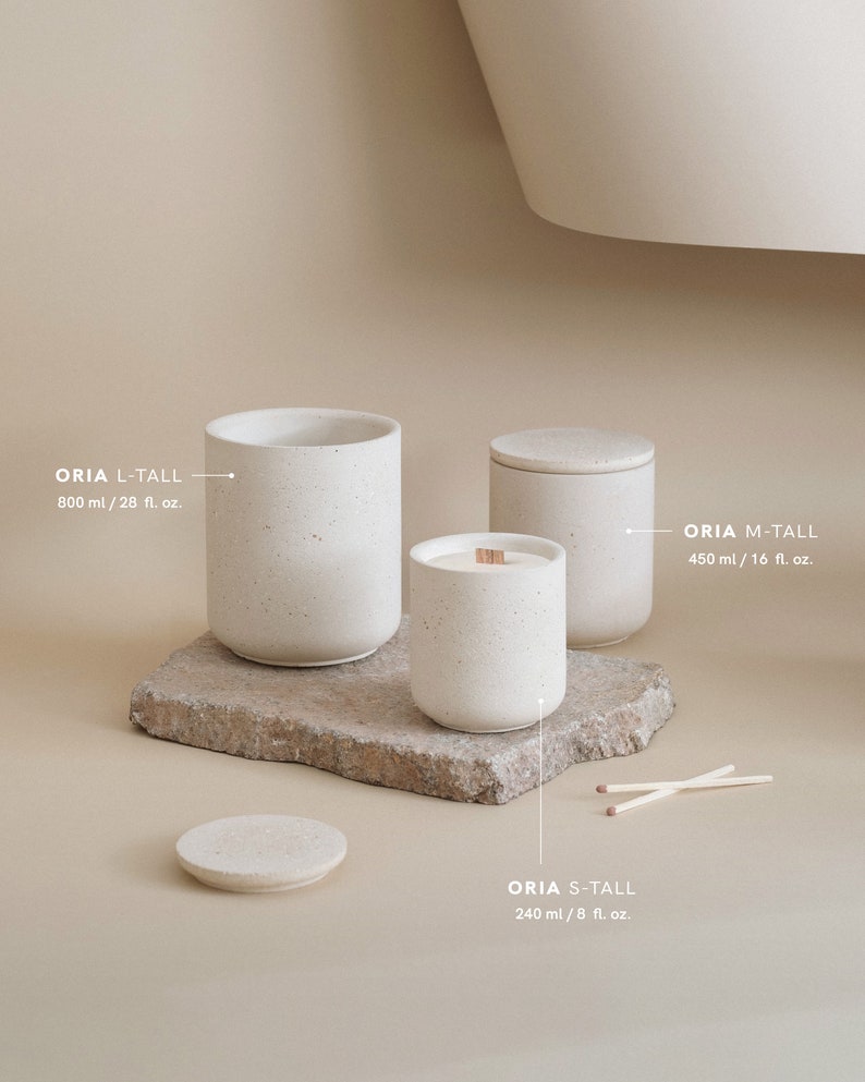 May include: Three white ceramic candles of varying sizes with wooden wicks. The candles are labelled "ORIA L-TALL 800 ml / 28 fl. oz.", "ORIA M-TALL 450 ml / 16 fl. oz.", and "ORIA S-TALL 240 ml / 8 fl. oz.".