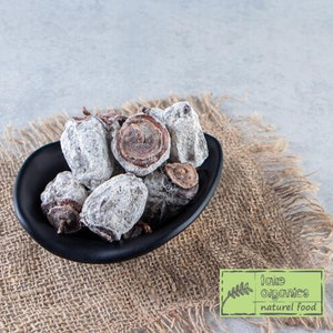 Puede incluir: Un bol negro lleno de caquis secos. Los caquis son de color marrón claro y tienen una capa blanca en polvo. El bol está sentado sobre un trozo de tela de arpillera.