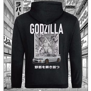 May include: Black hooded sweatshirt with a Godzilla graphic, a car, and Japanese text. The word "GODZILLA" is printed in white. The graphic is a detailed black and white illustration of the monster and a car in a city scene.