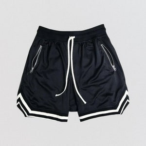 May include: Black athletic shorts with white trim around the bottom and sides. The shorts have a drawstring waist and zippered pockets.