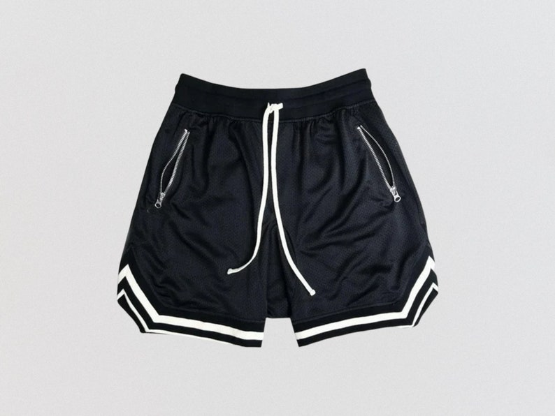 May include: Black athletic shorts with white trim around the bottom and sides. The shorts have a drawstring waist and zippered pockets.