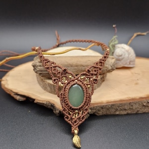 Peut inclure: Un collier en macramé marron avec un pendentif en pierre verte et un charme en feuille d'or.