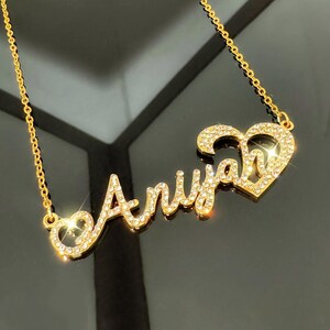 May include: Gold necklace featuring the name "Ariya" in cursive script with rhinestones and a heart charm.