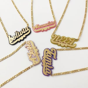 Può includere: Cinque collane con catena dorata e targhette con nomi personalizzati. Le targhette sono di diversi colori e hanno una finitura scintillante. I nomi sulle targhette sono "Bolivia", "Alexandria", "N&E&T", "Ashley" e "Olivia".
