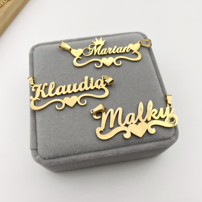 May include: Three gold-tone nameplate necklaces with a heart charm. The names are Marian, Klaudia, and Maliky.