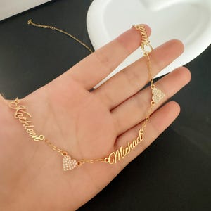 May include: Gold necklace with two cursive names, "Kathleen" and "Michael", separated by two heart-shaped charms with clear rhinestones.