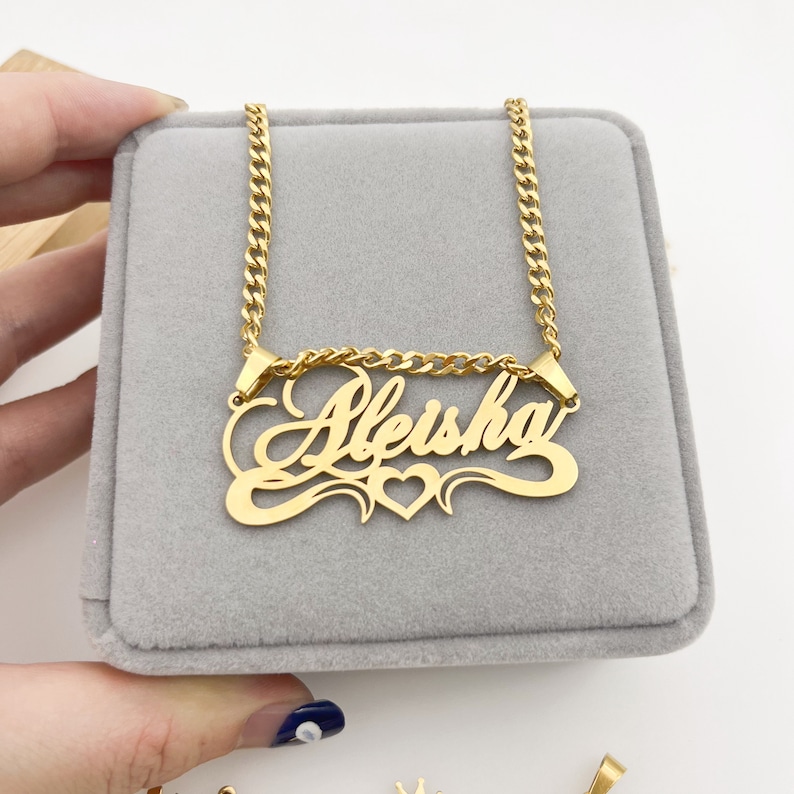 May include: Gold chain necklace with a cursive nameplate pendant that says "Aleisha" with a heart in the center.
