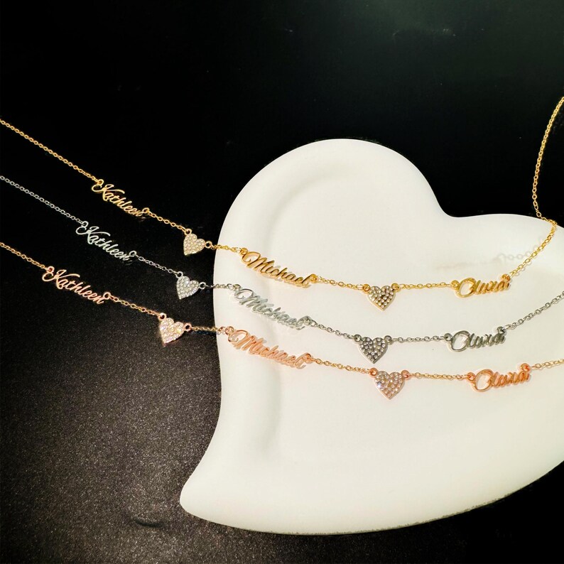 May include: Three gold, silver and rose gold necklaces with a heart charm and a name on each. The names are Kathleen, Michael and Olivia.