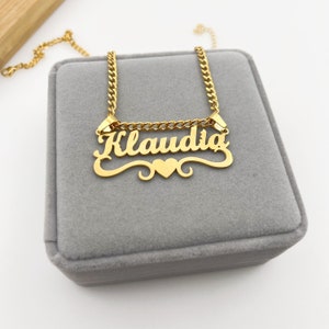 May include: Gold necklace with a nameplate pendant that reads "Klaudia" with a small heart charm. The necklace is on a gray velvet box.