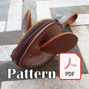 May include: A brown leather coin purse shaped like a rabbit, with a zipper closure and stitched detailing. The purse has two upright ears and a small handle. The word "Pattern" is displayed in white text. A PDF icon is in the corner.