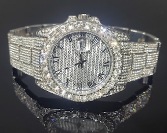 May include: A silver watch with a white face and Roman numeral hour markers. The watch is covered in clear rhinestones.