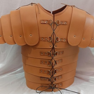 Può includere: Una corazza romana in pelle color cuoio, con piastre a strati e protezioni per le spalle. L'armatura è allacciata sul davanti con cordini di cuoio e fissata con fibbie e rivetti metallici. Il design ricorda l'abbigliamento militare storico.