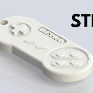 Peut inclure: Modèle 3D imprimé en plastique blanc d'une manette de jeu vidéo rétro avec un pavé directionnel, six boutons et le mot "RETRO" imprimé sur le dessus.