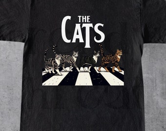 May include: Black t-shirt with a graphic of five cats walking across a crosswalk. The text "THE CATS" is above the cats.