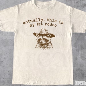 Actually, This Is My First Rodeo T-Shirt | Funny Western Graphic Tee | Raccoon Quote | Retro Shirt Unique Gift Idea | Unisex Shirt