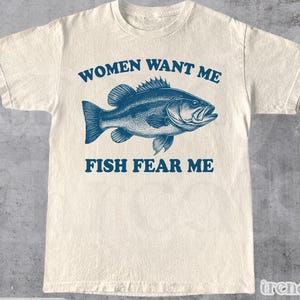 Peut inclure: Un t-shirt blanc avec un graphique bleu d'un poisson et le texte "Women Want Me Fish Fear Me".