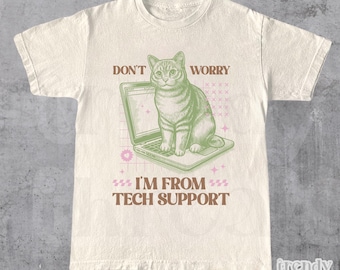 Könnte beinhalten: Ein beiges T-Shirt mit einer grünen Katze, die auf einem Laptop sitzt. Der Text auf dem Shirt lautet "Don't Worry I'm From Tech Support".