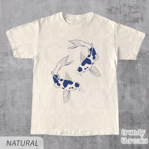 May include: A white t-shirt featuring a blue outline of two koi fish swimming in opposite directions. The fish have black spots and are on a natural coloured t-shirt. The text "trendy threads" is in the bottom right corner of the image.