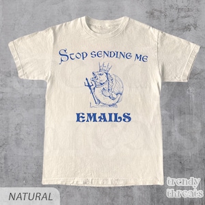 以下が含まれることがあります： 「Stop Sending Me Emails」というテキストと、王冠をかぶった魚がトライデントを持っている青いグラフィックが描かれた白いTシャツです。