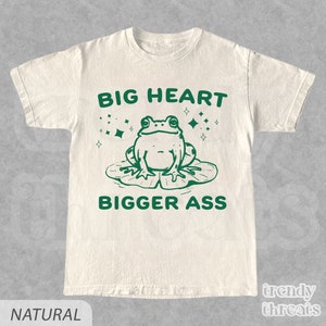 Op de afbeelding: Een crèmekleurig T-shirt met een groene kikkergrafiek en de tekst "BIG HEART BIGGER ASS".