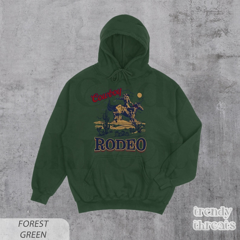 May include: Forest green hooded sweatshirt with a vintage-style illustration of a cowboy riding a horse. The text "Cowboy Rodeo" is printed in red and gold on the front of the sweatshirt.