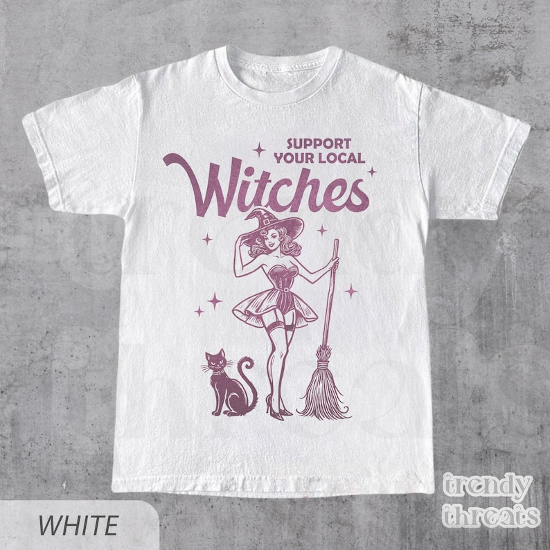 Flat lay white color shirt with quote 'Support Your Local Witches' and retro Halloween witch graphic.