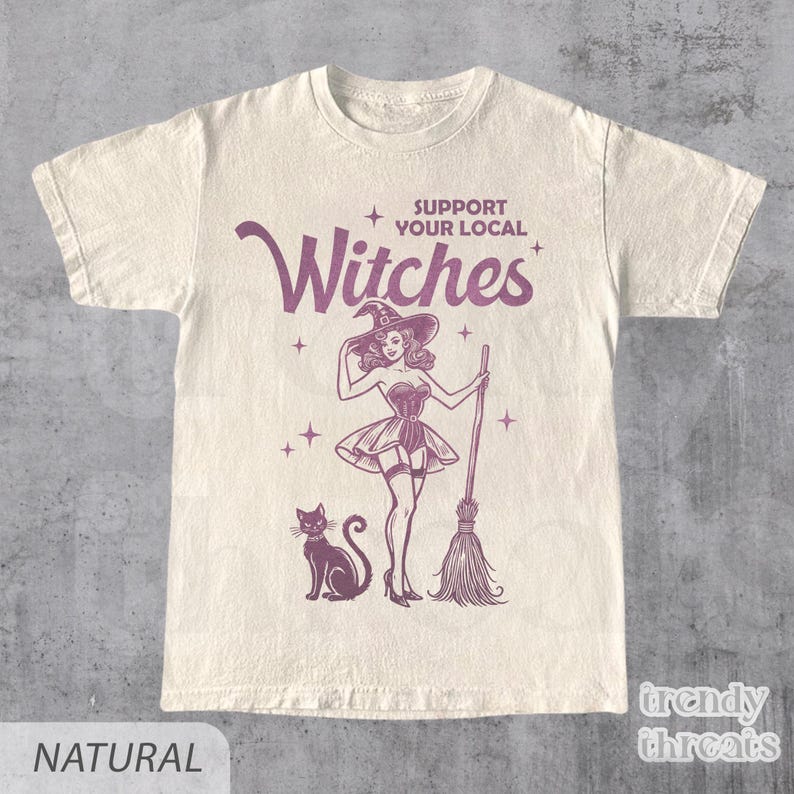 Flat lay ivory color shirt with quote 'Support Your Local Witches' and retro Halloween witch graphic.