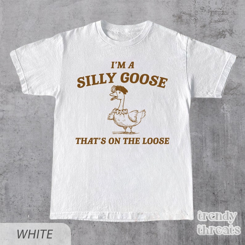 Op de afbeelding: Wit T-shirt met een bruine illustratie van een gans met een hoed en de tekst "I'm a Silly Goose That's on the Loose."