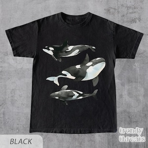 May include: Black t-shirt with a watercolor design of three orcas swimming. The orcas are black and white with a light blue wash.