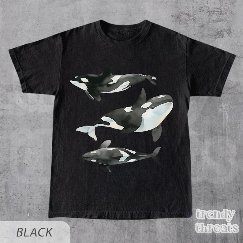 May include: Black t-shirt with a watercolor design of three orcas swimming. The orcas are black and white with a light blue wash.