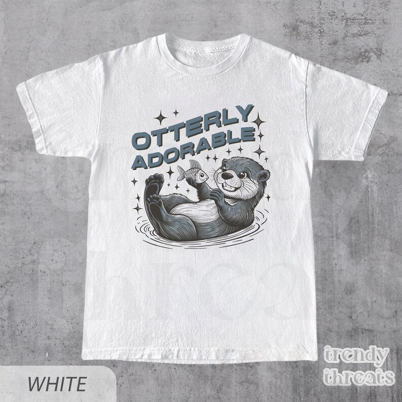 May include: White t-shirt with a graphic of an otter holding a fish and the text "Otterly Adorable".