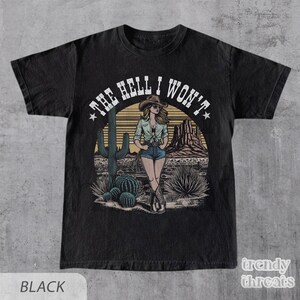 May include: Black t-shirt with a vintage-style graphic of a woman in a cowboy hat standing in a desert landscape. The text "THE HELL I WON'T" is written in a circle around the woman.