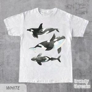 May include: White t-shirt with a graphic of three black and white orcas swimming. The text "trendy threads" is printed in the bottom right corner.