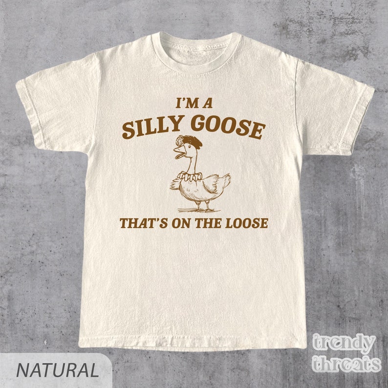 Op de afbeelding: Een beige T-shirt met een bruine afbeelding van een gans met een kroon en de tekst "I'm a Silly Goose That's on the Loose."