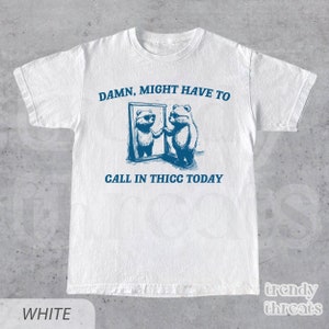 May include: White t-shirt with a blue graphic of two bears looking in a mirror. The text "DAMN, MIGHT HAVE TO CALL IN THICC TODAY" is printed on the shirt.