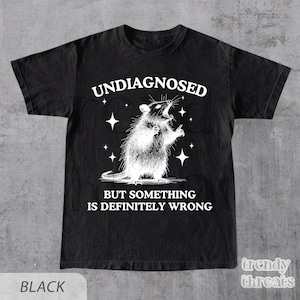 May include: Black t-shirt with a distressed graphic of a rat and the text "UNDIAGNOSED BUT SOMETHING IS DEFINITELY WRONG." The shirt also has a "trendy threats" logo in the bottom right corner.